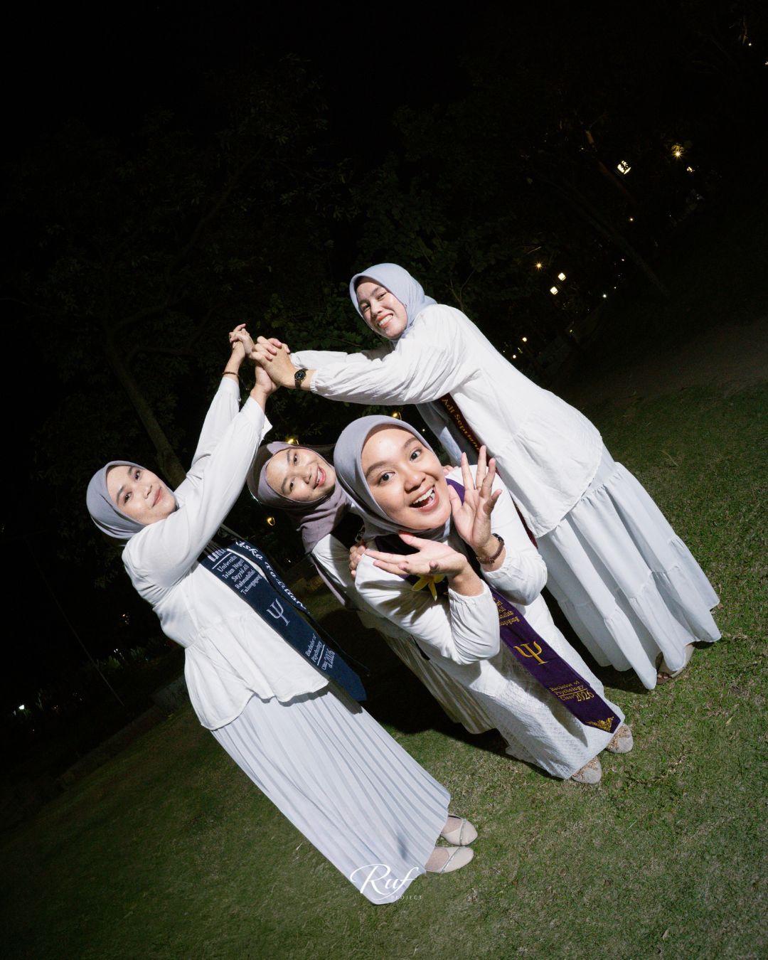 Sahabat wisudawati berpose ceria di rumput pada malam hari
